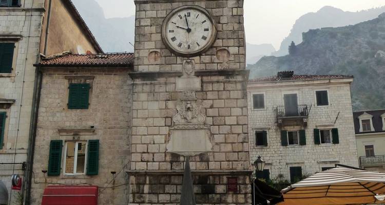 Torre del reloj en una plaza con edificios alrededor.