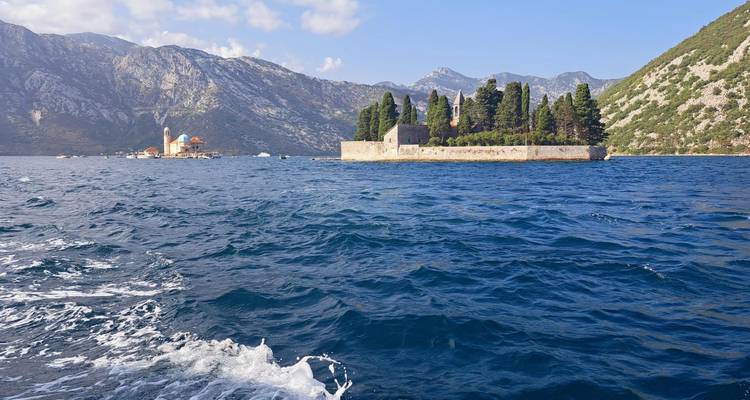Vista lejana de los islotes gemelos Nuestra Señora de las Rocas y Sveti Đorđe en medio de la reluciente Bahía de Kotor enmarcada por montañas escarpadas