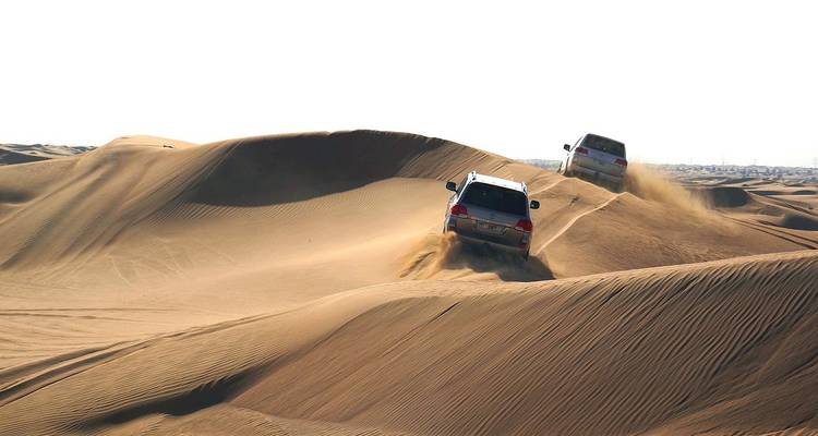 SUVs driving over sand dunes in desert.