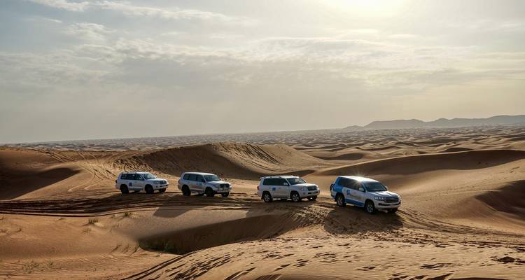 Four SUVs driving through sandy desert landscape.