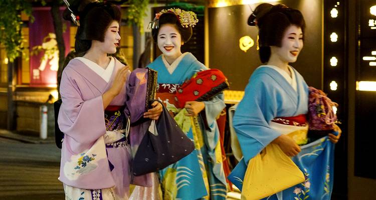 Drei Frauen, die als Geishas verkleidet sind, gehen nachts auf einer Straße.