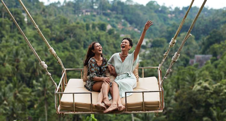 Dos mujeres disfrutando de un columpio sobre exuberante vegetación.