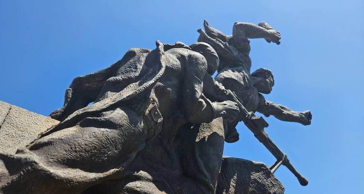 Dramatic upward view of a bronze resistance monument depicting fighters under a vivid blue sky