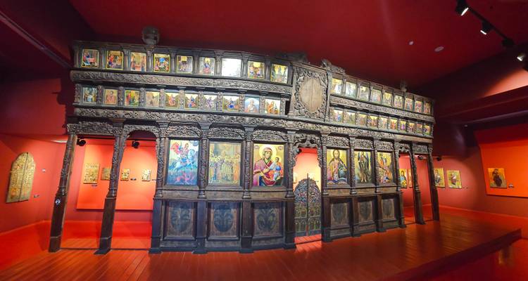 Wide interior of a red-walled museum displaying an ornate wooden iconostasis surrounded by religious paintings