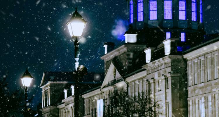 Scène nocturne d'un bâtiment avec dôme illuminé et lampadaires sous la neige qui tombe.