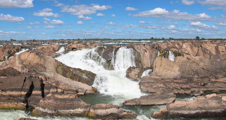 Wide waterfall surrounded by rocky terrain under a blue sky.