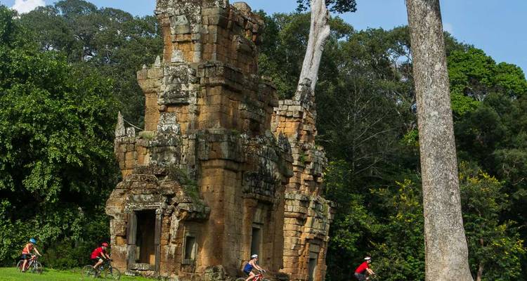 Cyclists passing by an ancient stone structure in the jungle.