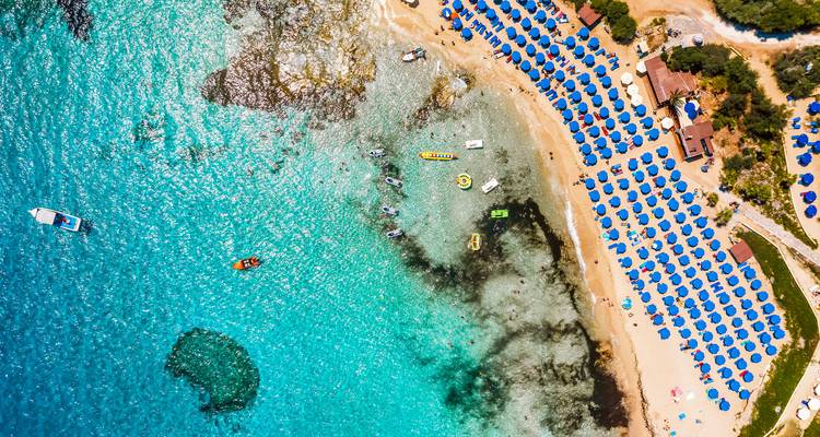 Vue aérienne d'une plage animée avec des parasols bleus et une eau claire.