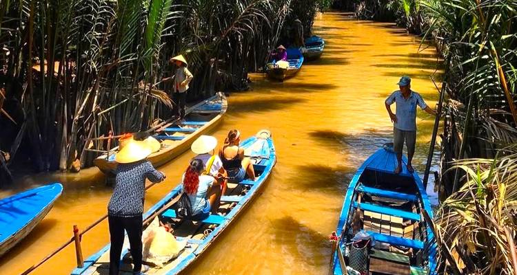 People paddling long boats in a dense jungle waterway.