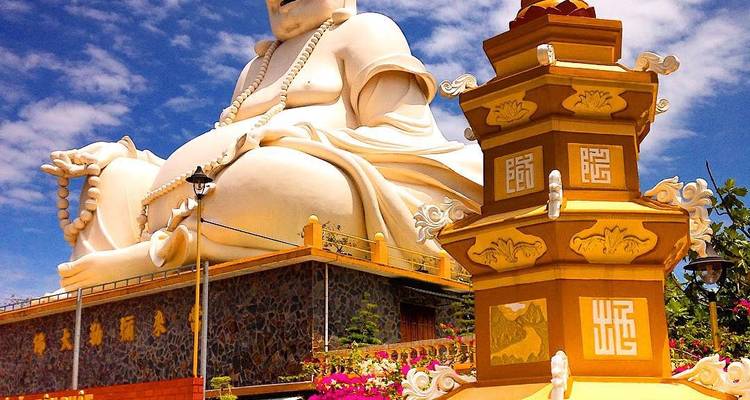 Large white Buddha statue at a temple complex under a clear blue sky.