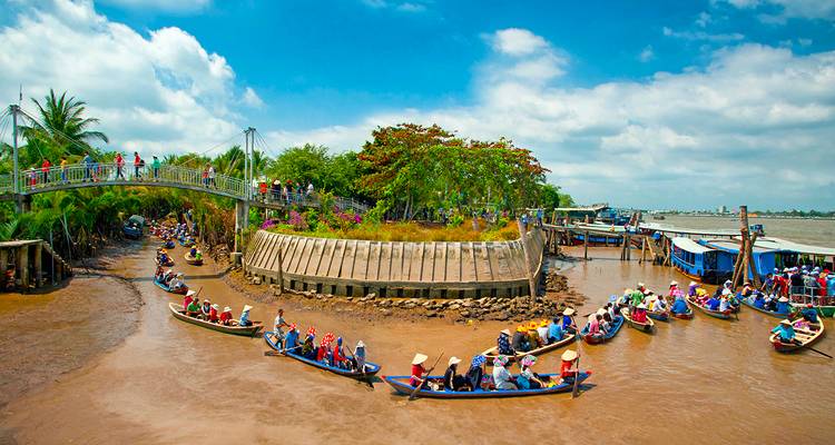 Numerous boats with people in a wide river with a bridge.