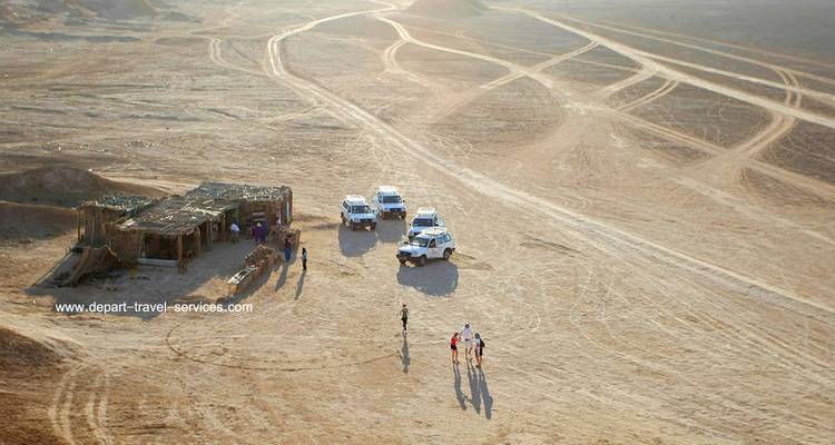 Vue aérienne de véhicules et de personnes dans une zone désertique, avec un filigrane visible.