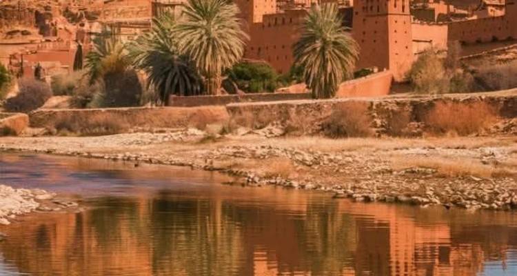 Ville fortifiée historique avec des palmiers reflétés dans une rivière.