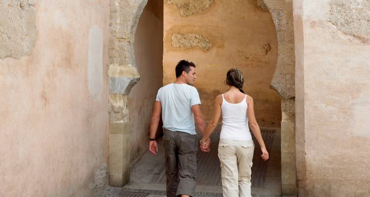 Young couple holding hands walking through a stone archway in an old medina alley.