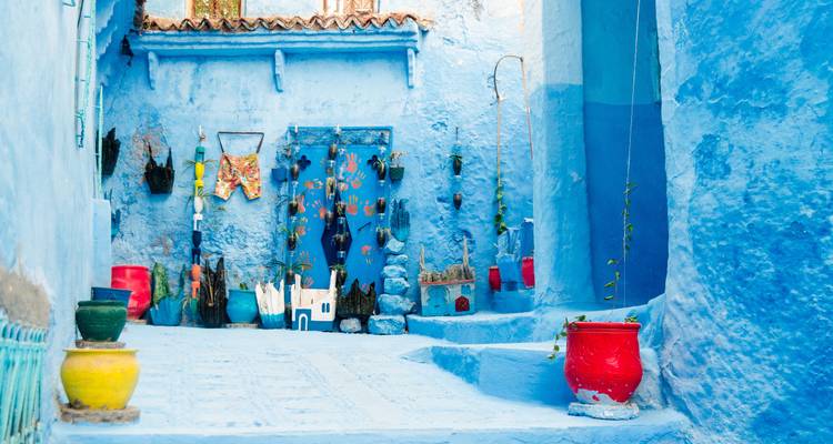 Pots colorés et plantes dans une ruelle bleue.