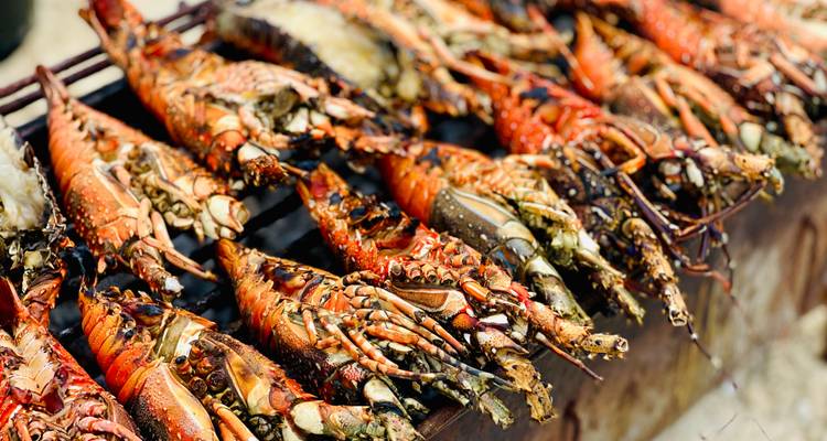 Rijen gegrilde kreeften die sissen op een barbecue, hun schalen feloranje en licht aangebrand.