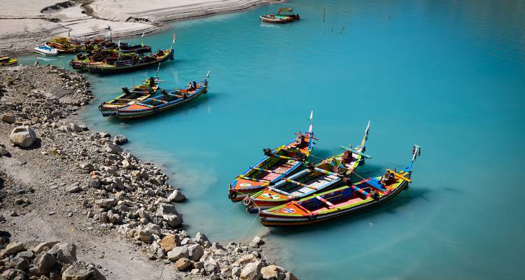 Brightly painted boats moored on vivid blue alpine lake beside rocky shoreline