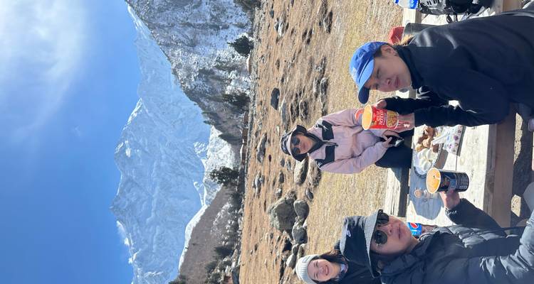 Friends enjoying instant noodles at picnic table with snowy mountains behind