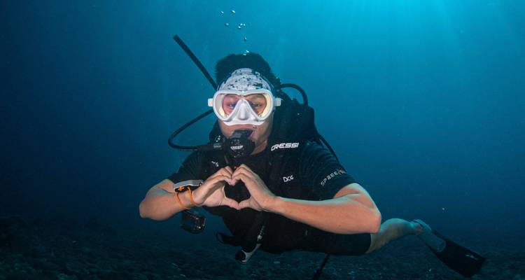 Plongeur sous-marin formant un cœur avec ses mains sous l'eau.
