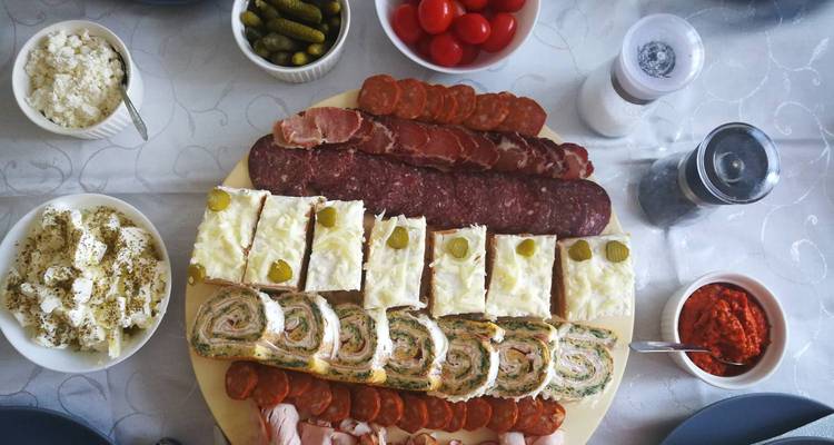 Home-style spread of cold cuts, cheeses, pickles and savory pastries on a dining table.