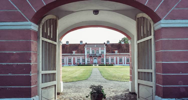 Un bâtiment rose vu à travers une arche avec un chemin qui y mène.