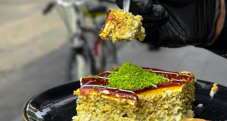Primer plano de un tenedor levantando un postre de pistacho cremoso rociado con jarabe y cubierto con nueces verdes.