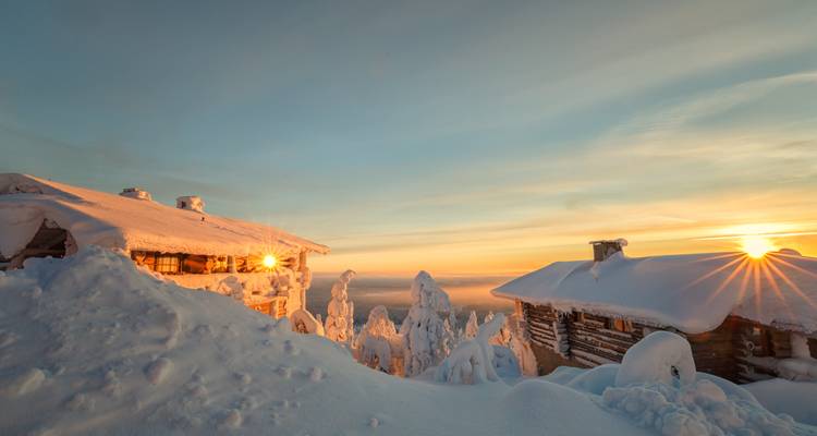 Cabanes couvertes de neige avec le lever du soleil se reflétant sur les fenêtres.