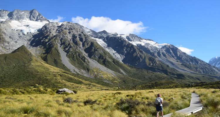 Excursionista en un sendero con montañas y glaciares al fondo.