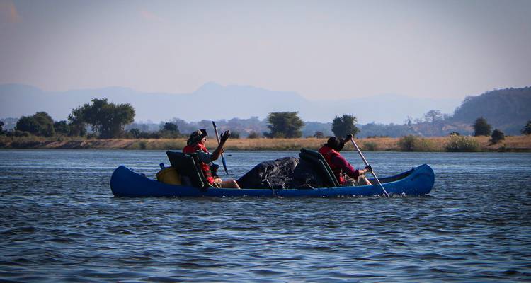 Twee reizigers peddelen met een uitgeruste kano over open water met bergen in de verte.