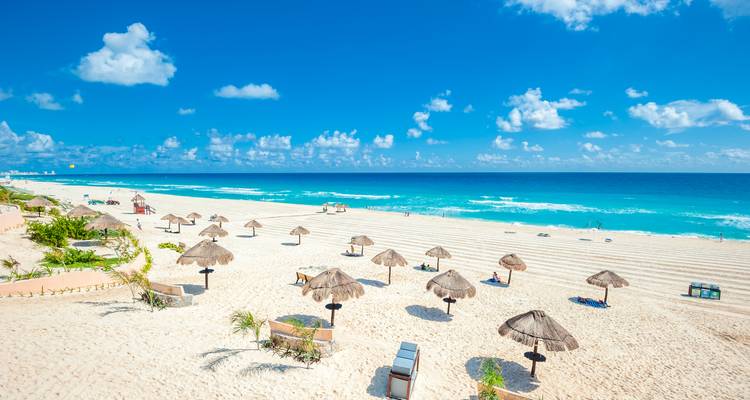 Sonniger Strand mit Strohdach-Sonnenschirmen und klarem blauen Himmel.