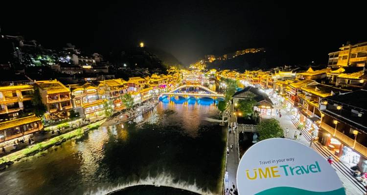 Vue nocturne d'une rivière avec des bâtiments traditionnels illuminés et un filigrane.