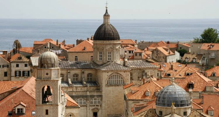 Stadsgezicht met koepelgebouwen en zee op de achtergrond.