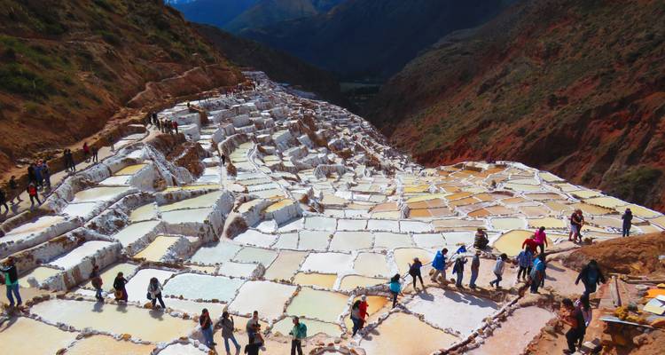 Die terrassenförmig angeordneten weißen Salzbecken von Maras erstrecken sich über einen Andenhang, während Touristen die Gegend erkunden.