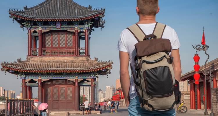 Un voyageur avec un sac à dos se tenant devant une architecture chinoise traditionnelle.