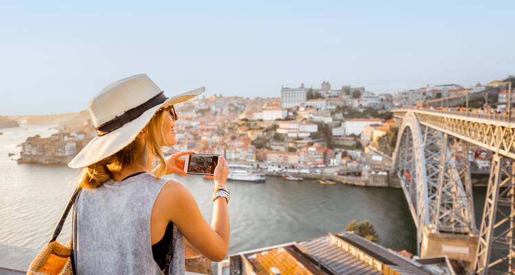 A woman taking a photo of a cityscape with a bridge.