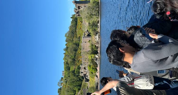 Touristen auf einer Bootsfahrt fotografieren die Ruinen von Urquhardt Castle über Loch Ness.