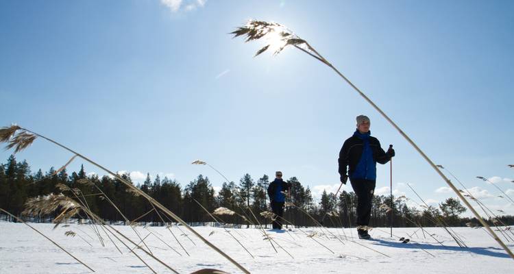 Deux personnes skient sur un terrain enneigé sous un ciel lumineux.