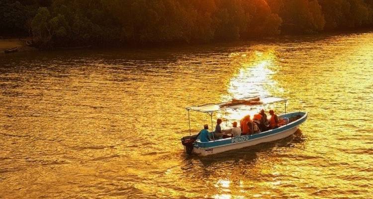 Un petit bateau avec des gens qui profitent d'un coucher de soleil doré sur une rivière