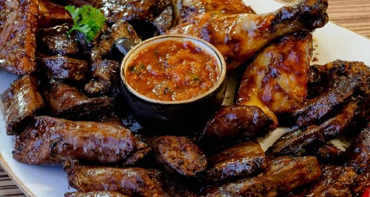 Verschiedene gegrillte Fleischsorten und Sauce auf einem Teller.