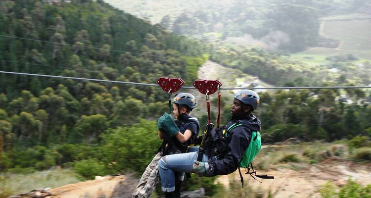 Zwei Personen beim Ziplining in einem bewaldeten Gebiet.