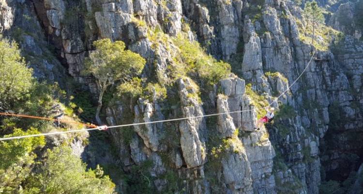 Person überquert ein Hochseil zwischen felsigen Klippen.
