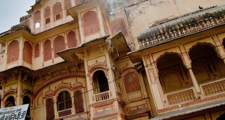 Antiguo haveli rajastani con arcos ornamentados y pintura pastel descolorida iluminada por la luz del sol.