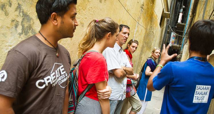 Un pequeño grupo de turistas escucha a un guía local en un callejón histórico y estrecho.