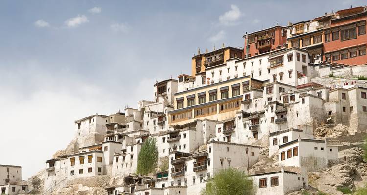 Cluster of whitewashed monastery buildings climbing a rugged mountainside beneath a pale sky.