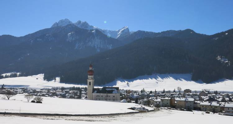 Snowy valley with town and prominent snow-capped mountain in the background.
