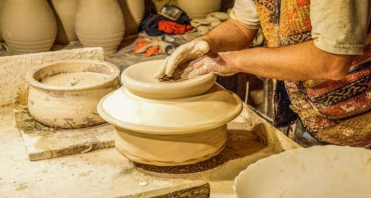 Tour de potier façonnant l'argile en pot, mains visibles.