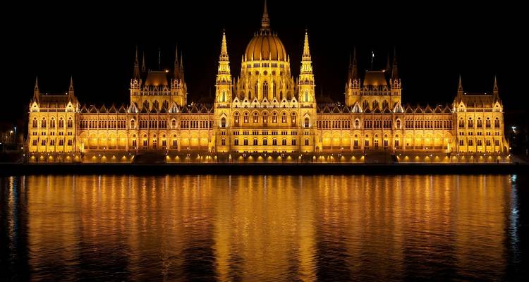 Bâtiment du parlement de Budapest illuminé la nuit avec des reflets sur l'eau.