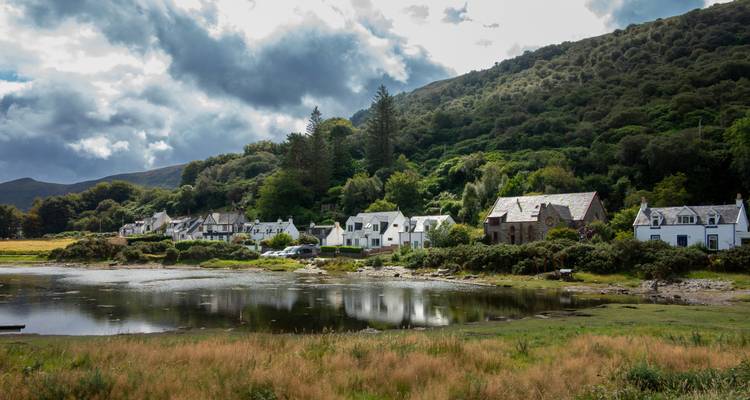 Küstendorf mit weißen Häusern, eingebettet vor der Kulisse eines bewaldeten Hangs.