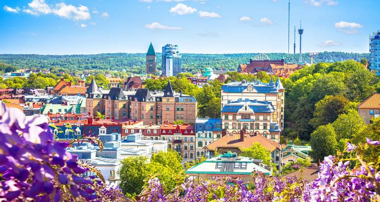 Colourful rooftops and spires poke through lush summer greenery in Gothenburg viewed from an elevated garden.