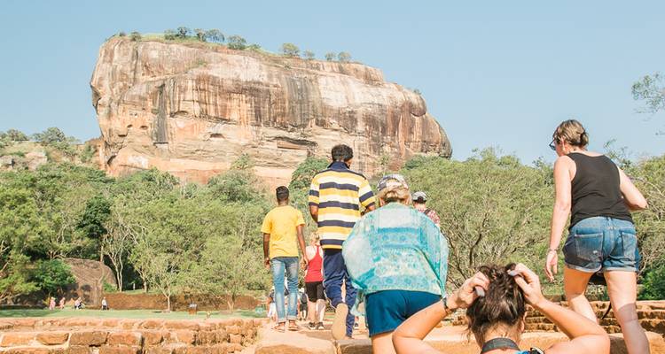 Des touristes marchant vers le rocher de Sigiriya au milieu des arbres et sous un ciel dégagé.